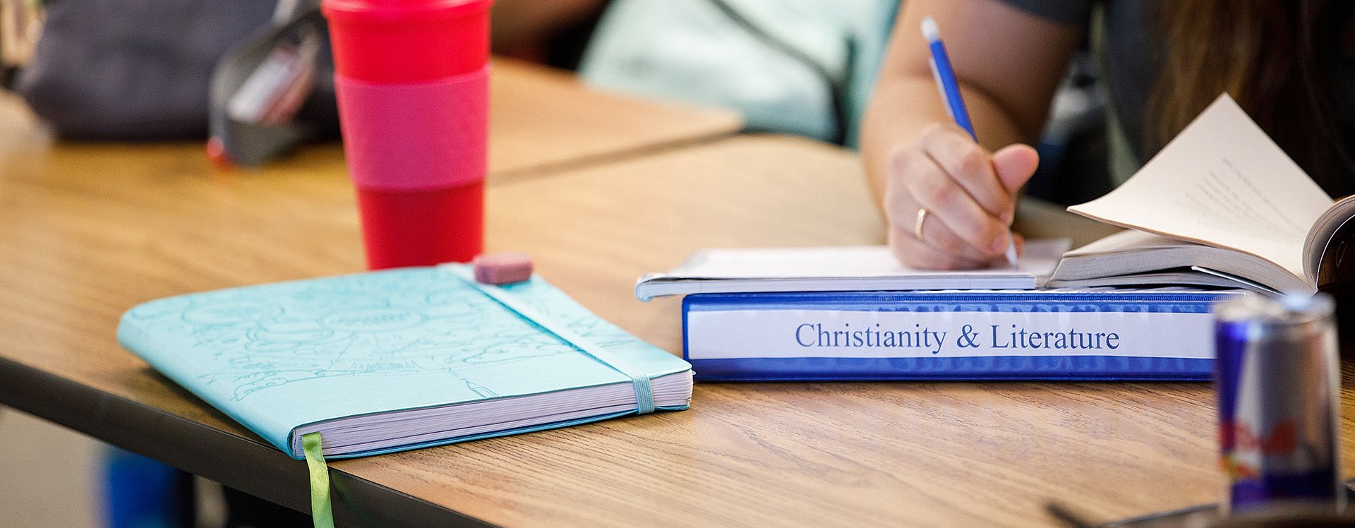 desk with cup and notebooks, one labeled Christianity and Literature