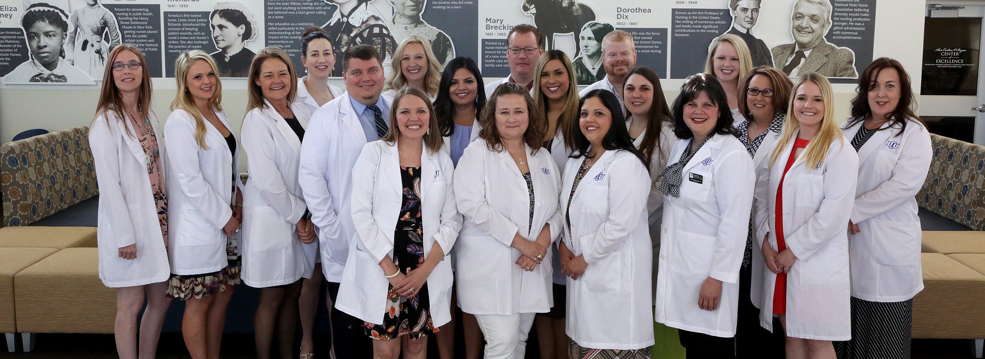 A group of graduate nursing professors in white coats posing for a professional photo in the Margaret Talkington Building