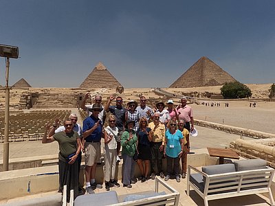 A group of individuals posing in front of the pyramids, proudly holding up the chap symbol with their hand for the photo