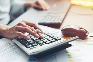 Someone is at a desk set up with a keyboard, mouse, calculator, and some loose papers, as the woman relaxes her left hand and types on the calculator with a pencil in her left hand