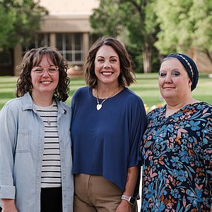 Photograph of three women, all employees of the Student Business Office, standing outside smiling at the camera