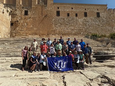 A group of individuals posing in front of a Temple in Jerusalem holding a LCU flag