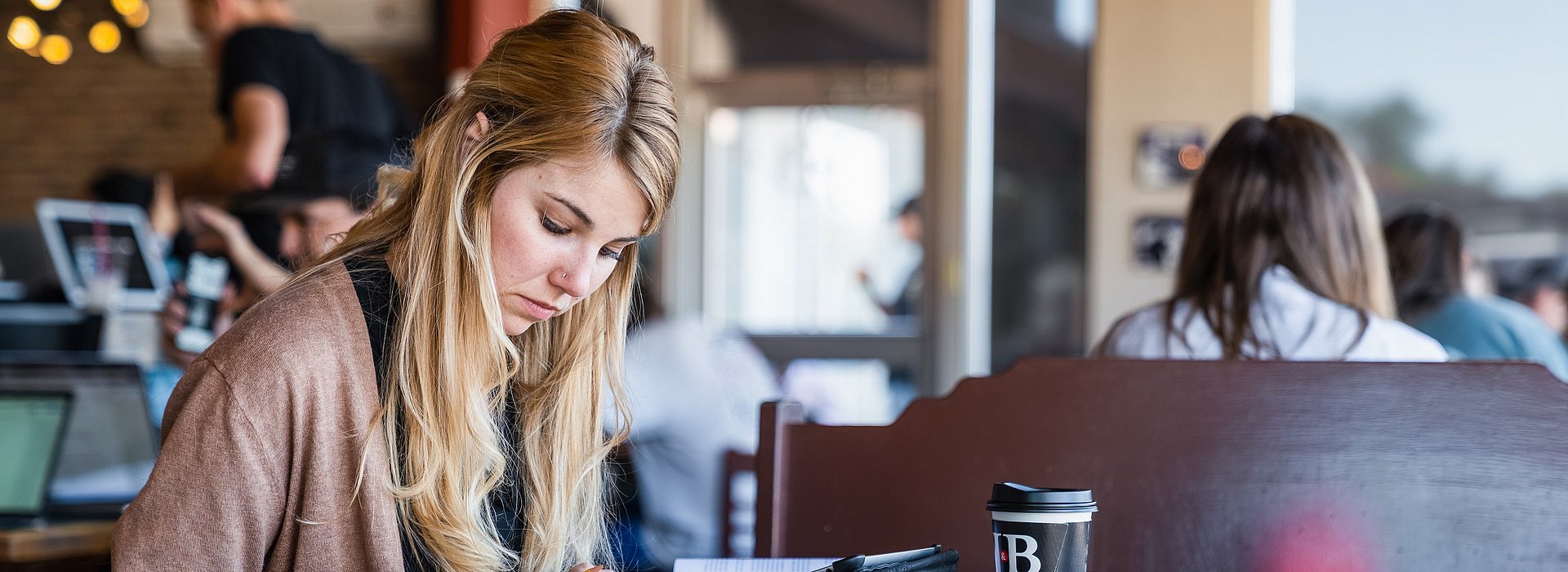Girl reading through a book taking notes at table in a coffee shop