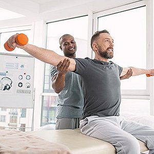 Physical therapist helping patient lift arms out while holding dumbbells