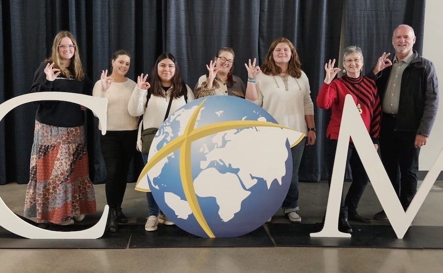LCU mission trip with staff and students standing behind a sine reading "ICOM" with the "O" looking like a globe with a cross over it
