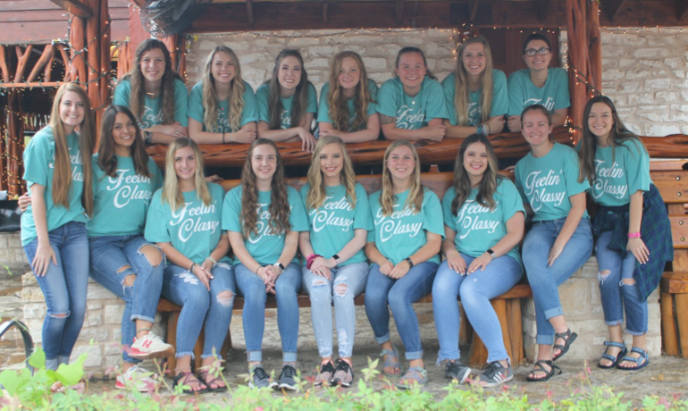 A group of girls gathering around a wooden seat all with jeans and a teal shirt with the words feeling classy on them