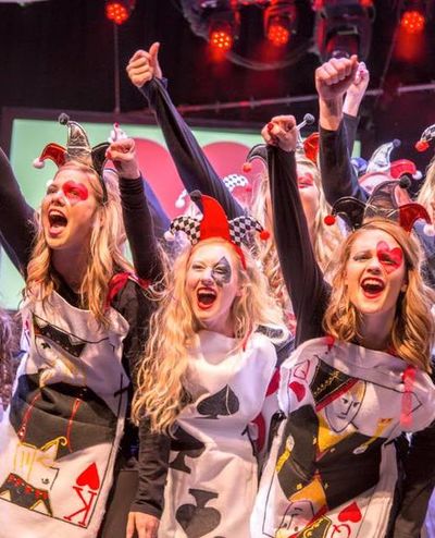 A group of girls at the end of a Follies show with their fists up in the air as they are screaming with a deck of cards as their costumes