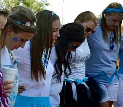 A group of girls gathered around in a huddle as they pray